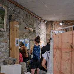 Des gens dans une pièce aux murs en pierre où on voit des photos, une peinture, des éléments d'architecture ancienne, un panneau Dinosaures, un plan.