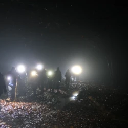 Des marcheurs de nuit avec lampes frontales en file indienne dans le brouillard formant des halos autour des lumières.