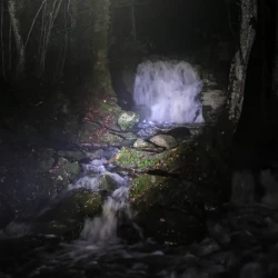 La cascade éclairée par des lumières bleues de lampes leds au milieu des bois.
