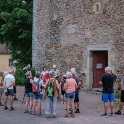 Un groupe de personnes autour d'une table qui boivent un verre et grignotent au pied d'une tour en vieilles pierres. En arrière plan de la végétation et un autre bâtiment ancien.