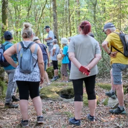 Des personnes en pause autour d'un trou d'eau formé dans la roche. Les bords sont moussus, on distingue de l'eau dans le trou.